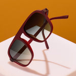 Red sunglasses with dark lenses on a white surface against an orange background