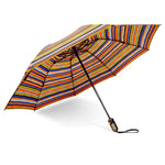 A vibrant striped collapsible umbrella stands open on a white background, featuring a pattern of varied horizontal bands in orange, blue, yellow, and black, with a contrasting gray handle and prominent orange push-button