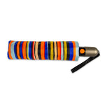 Folded umbrella with vivid vertical stripes in orange, blue, black, and yellow, featuring a dark grey handle and an orange auto-open button on a clean white background
