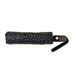 A folded umbrella on a white background featuring a black fabric with a white geometric line and dot pattern, a brown handle with a white push-button, and a black wrist strap