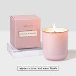 Pink scented candle in a glass jar with a lit wick next to its matching pink product box