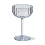 A clear ribbed champagne coupe glass with a tall stem and round base, showing subtle blue reflections on its polished surface