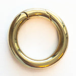 Photograph of a polished gold-colored O-ring spring gate clasp featuring a smooth perfect circular shape and a clear hinged opening against a stark white backdrop
