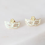 Gold-toned metal and crystal earrings featuring a pair of sparkling masquerade masks embellished with clear rhinestones and a subtle gold floral accent on a light surface