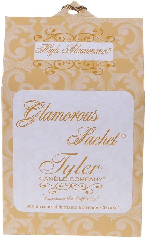 Tyler Candle Company's "High Maintenance" Glamorous Sachet product box features a rich golden yellow background with elegant white scrollwork patterns, a prominent white label with "Glamorous Sachet" in ornate gold script, and a decorative braided gold hanging loop at the top