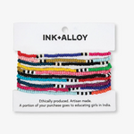INK+ALLOY seed bead bracelets a stack of vibrant multicolored thin bracelets featuring solid and striped patterns in a diverse spectrum of colors displayed on a white brand card detailing ethical production and support for girls' education in India