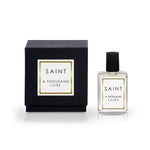 Product photograph showing a black perfume box with a gold-framed white label and a clear glass perfume bottle with a black cap, both featuring the text SAINT A THOUSAND LILIES, on a reflective white surface