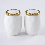 Two gleaming white ceramic salt and pepper shakers featuring decorative gold beaded rims, one shaker with three holes and the other with two, all on a bright white studio background
