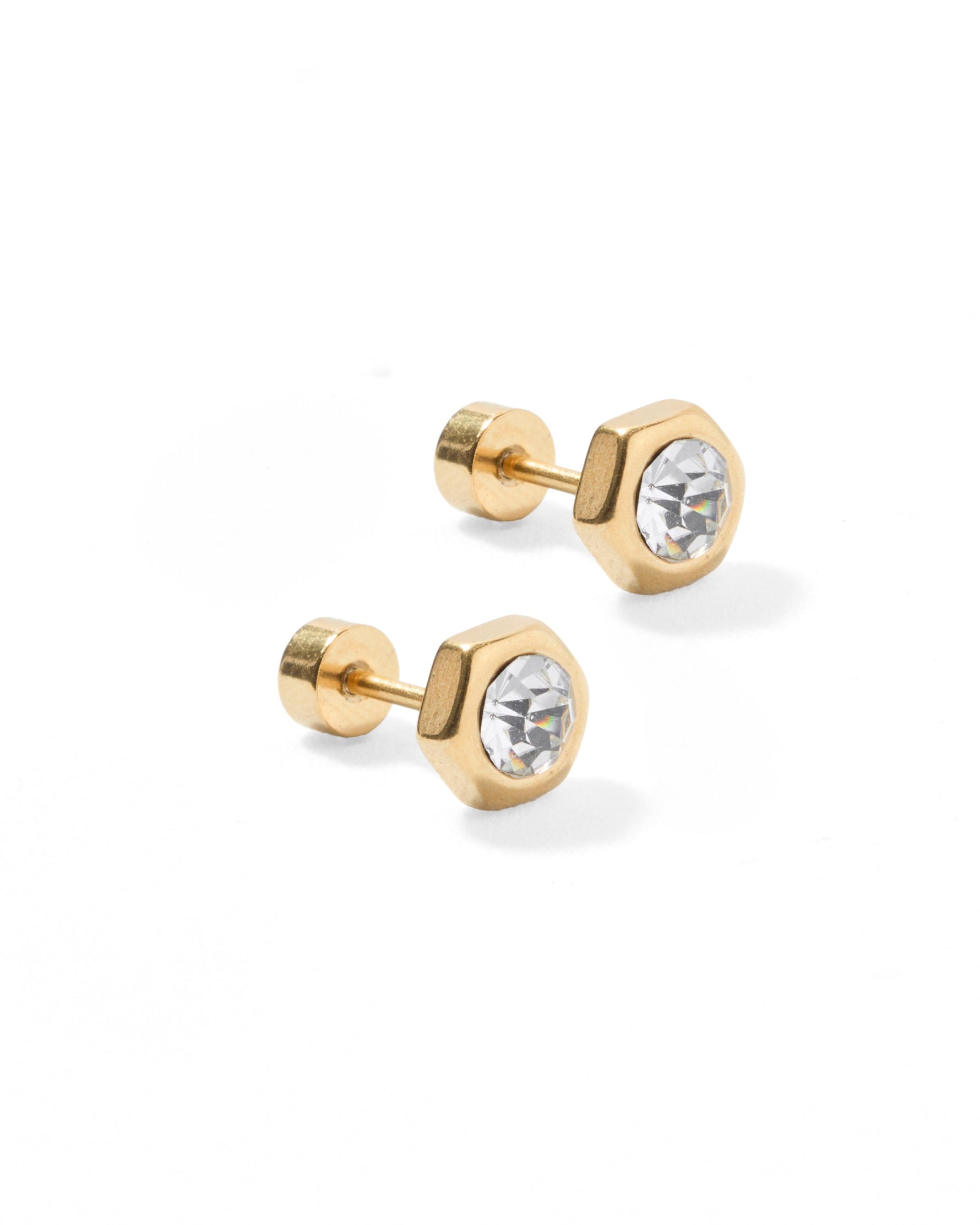 Photograph of a pair of gold-toned hexagonal stud earrings on a white background, each featuring a clear faceted crystal and a flat screw-back post