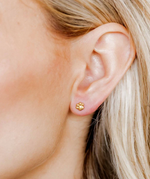 Photograph of a woman's ear adorned with a small golden paw print stud earring against fair skin with blonde hair visible
