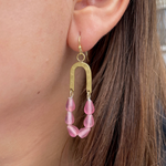 Handcrafted brass jewelry earring worn on a woman's ear featuring a textured hammered metal arch and a colorful strand of frosted pink teardrop-shaped glass beads