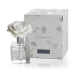 A Seychelles Gardenia reed diffuser featuring a white ceramic flower top on a clear square glass bottle, placed next to its white box with subtle grey floral patterns and branding