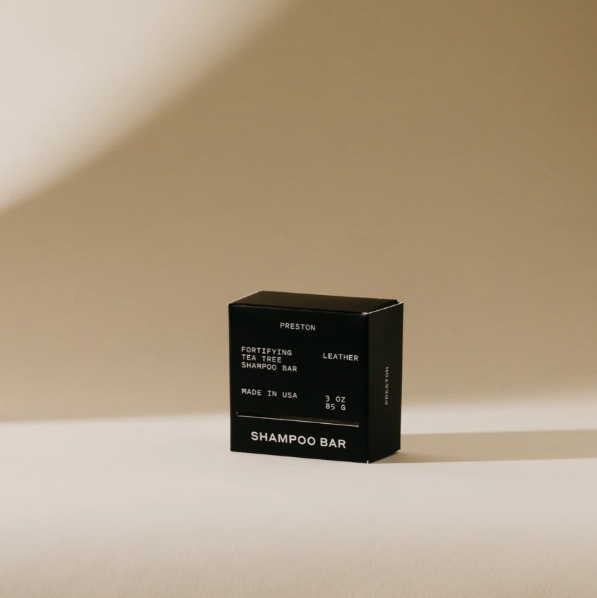 Product photography of a black Preston Fortifying Tea Tree Shampoo Bar box with minimalist white text including 'Leather' and 'Made in USA', presented on a light beige studio background with a soft shadow
