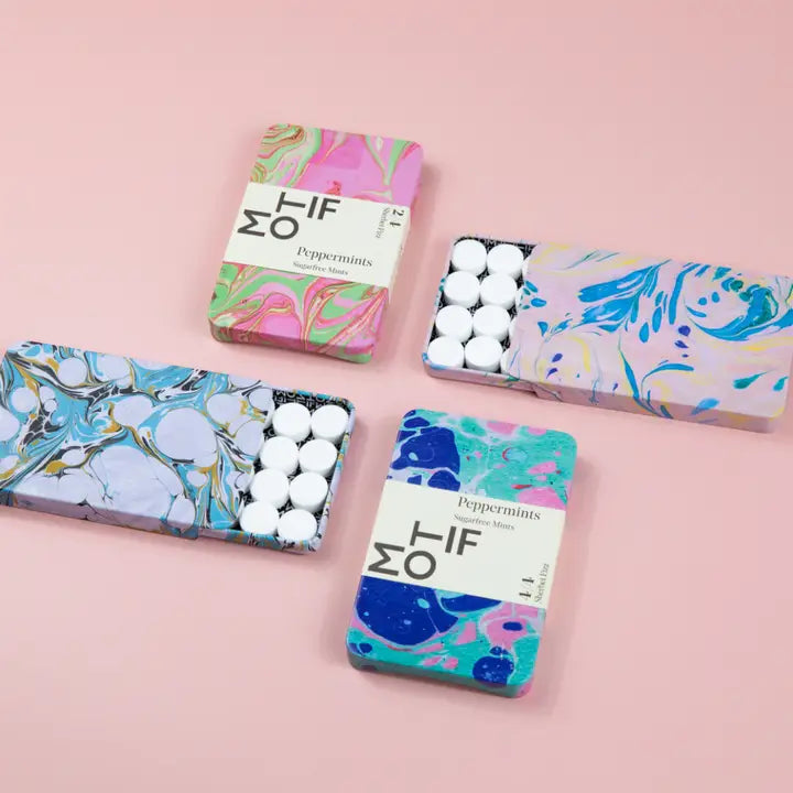 Four MO-IF Peppermints sugarfree mint tins featuring vibrant marbled designs in shades of pink, green, blue, and yellow, with two tins open revealing white round mints on a light pink surface
