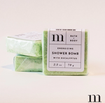 Product photography of three green 'm BATH + BODY' Energizing Shower Bombs with Eucalyptus, individually wrapped in clear plastic with white labels detailing 2.5 oz 70 g, displayed on a clean white background