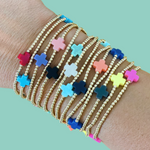 Photograph of a wrist adorned with multiple gold beaded bracelets, each featuring a colorful cross charm in a variety of vibrant and pastel hues including red, pink, and light blue