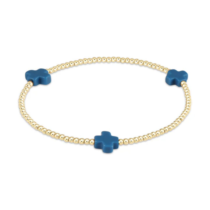 A gold beaded stretch bracelet featuring three evenly spaced matte teal blue cross-shaped beads on a white background
