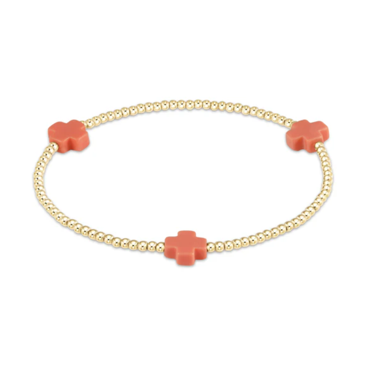 Jewelry: A delicate gold beaded stretch bracelet featuring three vibrant coral-colored cross-shaped accents