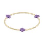 Jewelry gold beaded stretch bracelet with three matte lilac purple cross charms on a white background