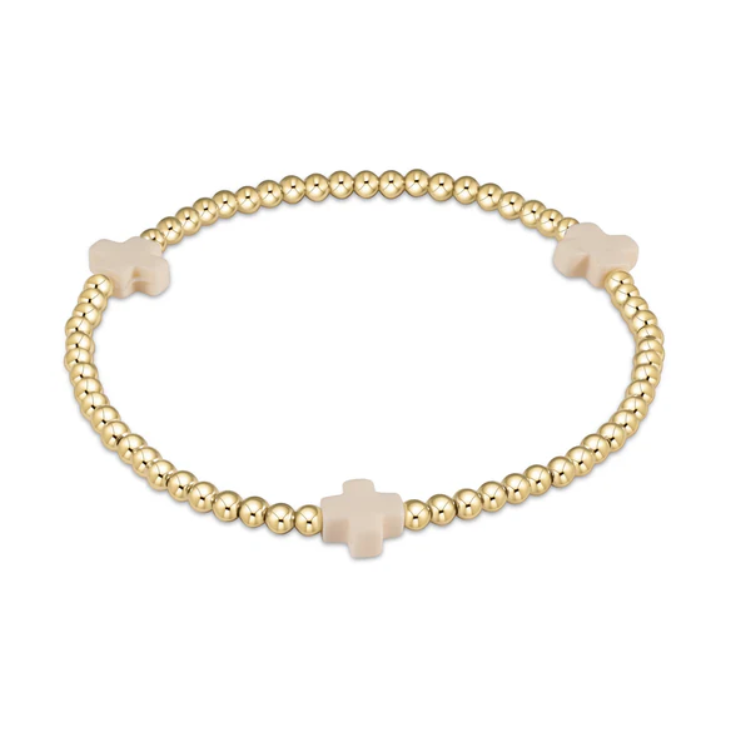A gold beaded stretch bracelet on a white background featuring three evenly spaced light pink cross charms