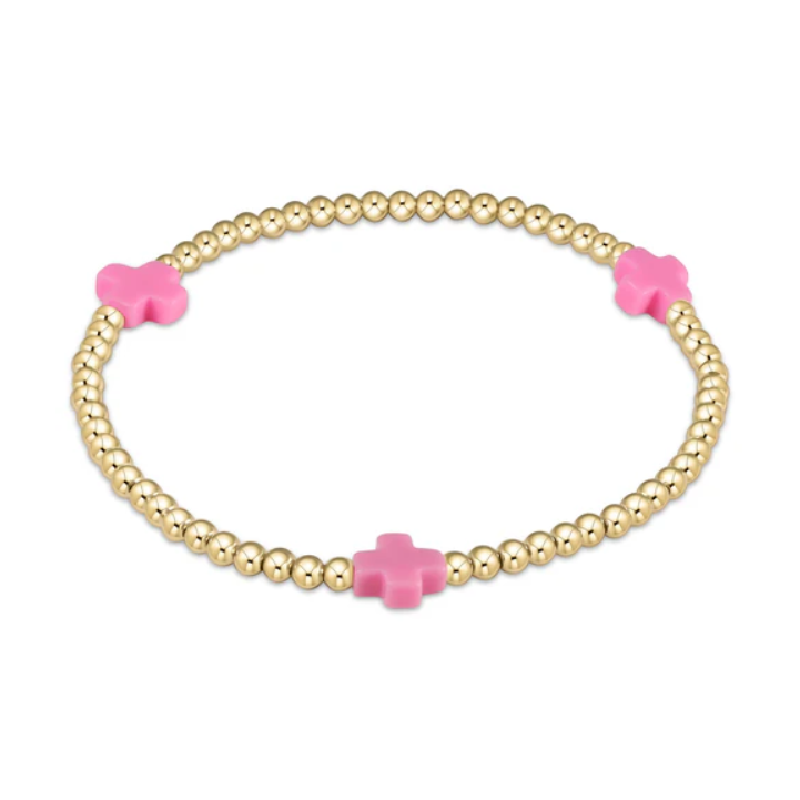 A gold beaded stretch bracelet features three vibrant pink cross-shaped charms on a pristine white background