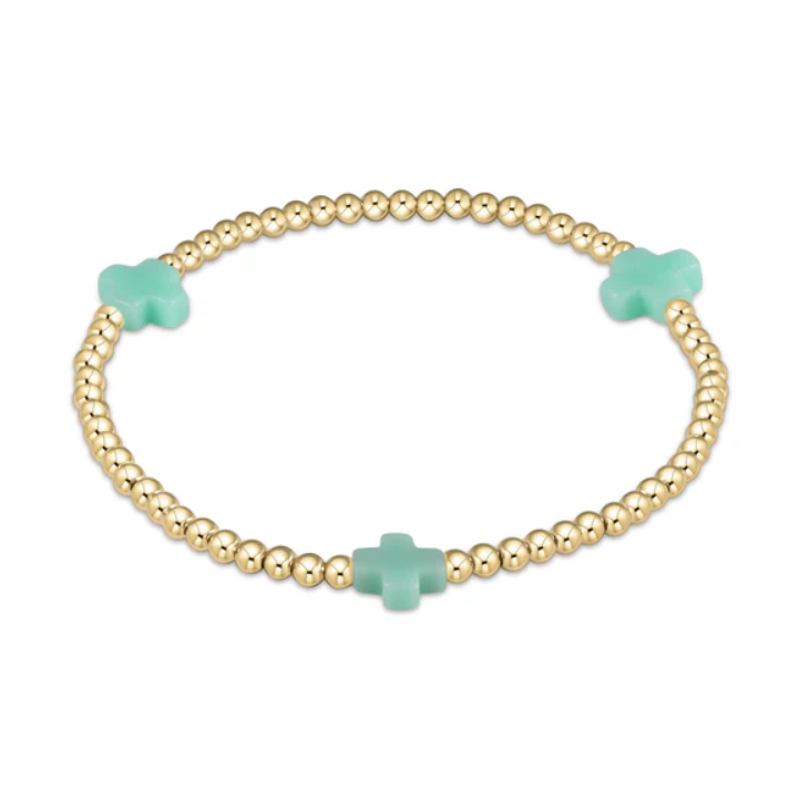 A gold-tone beaded elastic bracelet featuring three spaced mint green cross-shaped beads on a white background