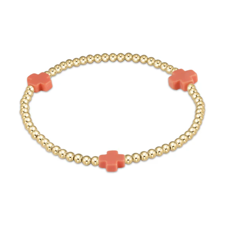 Gold beaded bracelet with three coral cross charms on a white background