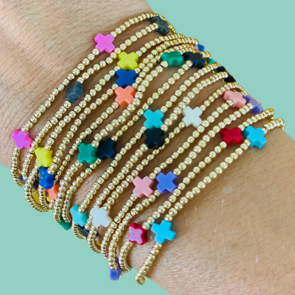 Stack of gold beaded bracelets with colorful cross shaped beads on a wrist