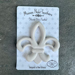Maison Nola silicone baby teether designed in New Orleans, featuring a light gray fleur-de-lis shape on white packaging with a repeating gray fleur-de-lis pattern over a dark textured background