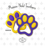 Digital product image by Maison Nola Teethers presenting two New Orleans-inspired vibrant purple and gold paw print baby teethers, one showing its textured reverse side with dots and spirals, on a background of subtle fleur-de-lis patterns