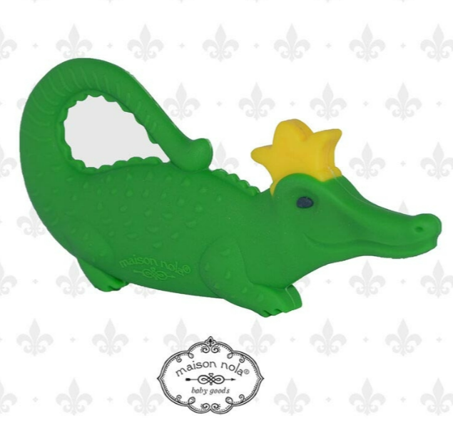 Silicone Maison Nola green alligator teether with a yellow crown and textured body, featuring a looped tail handle and subtle fleur-de-lis background representing New Orleans