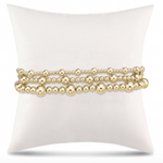Three strands of highly polished gold bead bracelets in varying sizes displayed on a soft white cushion