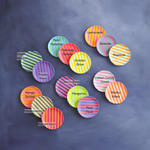A vibrant collection of circular striped coasters in various bright colors like pink, orange, yellow, green, and purple, each labeled with a playful name such as Lemonade, Flamingo Splash, and Purple Rain, arranged on a dark gray surface