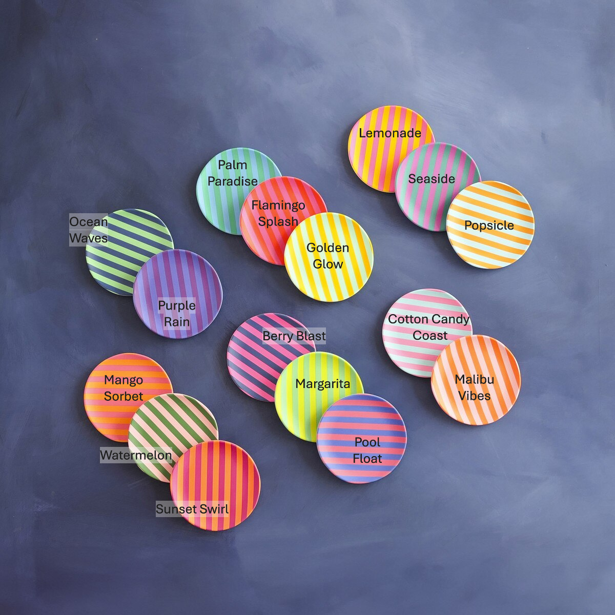 A vibrant collection of circular striped coasters in various bright colors like pink, orange, yellow, green, and purple, each labeled with a playful name such as Lemonade, Flamingo Splash, and Purple Rain, arranged on a dark gray surface