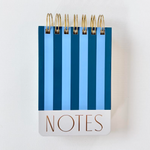 A spiral-bound notebook featuring a blue and dark blue striped cover, gold coil binding, and a white bottom band with copper-colored "NOTES" lettering