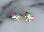 Enamel and gold-plated unicorn stud earrings featuring white bodies with pink tails, blue manes, and yellow horns on a white marble surface