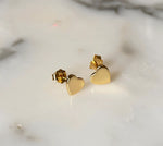 Pair of shiny gold heart stud earrings featuring a 925 stamp displayed on a white marble surface