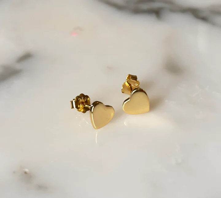 Pair of shiny gold heart stud earrings featuring a 925 stamp displayed on a white marble surface