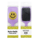 Product photography of two Mavi Bandz Style & Smile lavender paddle brushes in clear retail packaging, one adorned with a prominent gold glitter smiley face, the other displaying black bristles with white polka dot tips, resting on packaging featuring a yellow repeating smiley face pattern and text