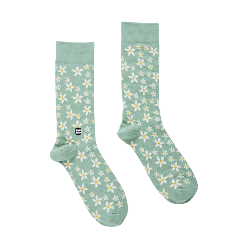 A pair of mint green socks patterned with white daisy flowers featuring yellow centers and a small black embroidered tram icon on the left sock