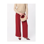 Person wearing beige sweater and red wide leg trousers holding a beige studded crescent handbag