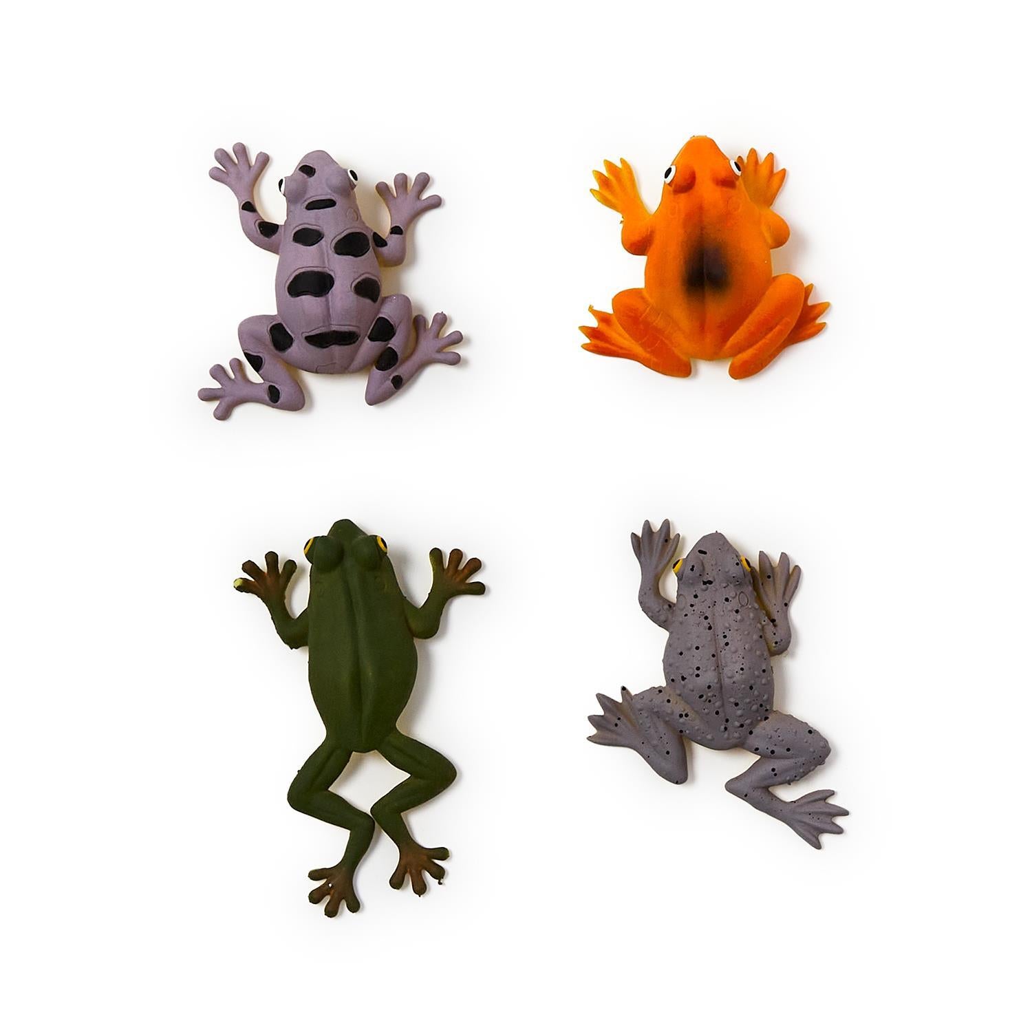 Molded plastic toy figurines of four colorful frogs on a white background featuring a lavender frog with large black spots, a vibrant orange frog, and a grey frog with textured speckles