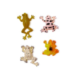 Plastic toy figurines of four colorful frogs on a white background featuring a pink frog with large black spots, a speckled cream frog, and a vibrant yellow-orange gradient frog