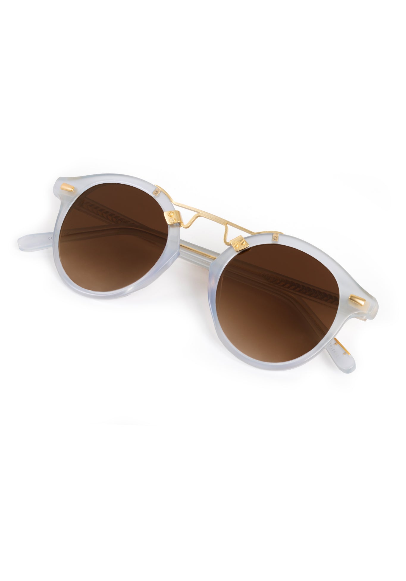 A pair of stylish sunglasses featuring translucent light blue acetate frames with brown gradient lenses and gold metal double bridge and rivet details on a clean white studio background