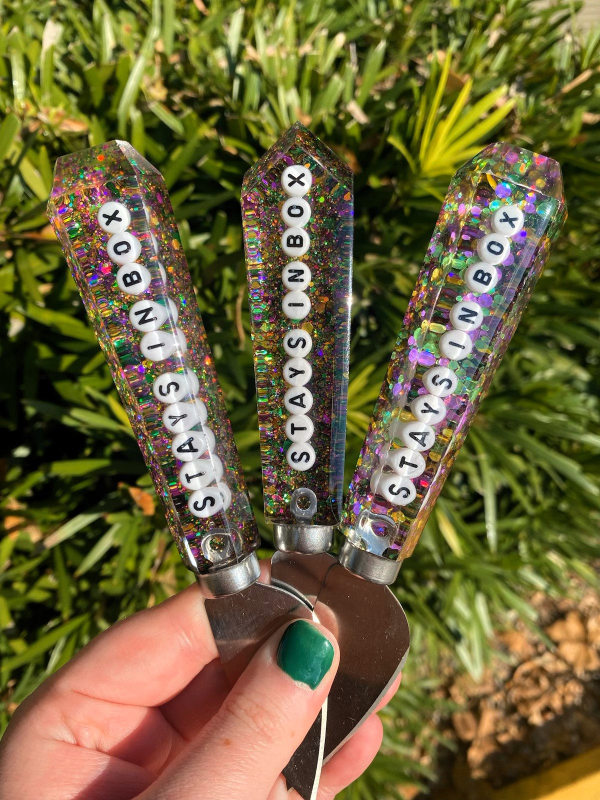 Three resin letter openers with colorful glitter and the text Stays In Box