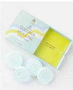 Product shot of Musee Coconut Milk & Fig Shower Steamers box, light blue with wavy yellow accents, open to reveal a chartreuse green interior and four light blue circular steamers with an embossed leaf logo
