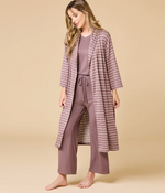 Studio photograph of a woman in a minimalist studio wearing a mauve three-piece loungewear set featuring a long striped robe and matching drawstring pants against a neutral beige background