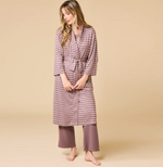 Digital photograph of a blonde model in a minimalist beige studio wearing a mauve belted robe with white horizontal stripes and matching wide-leg trousers