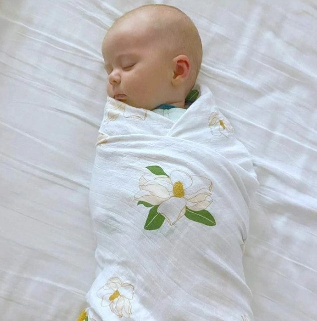 Baby swaddled in a white muslin blanket with a magnolia flower print