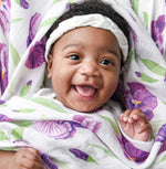 Baby wearing a white headband wrapped in a white blanket with purple floral print